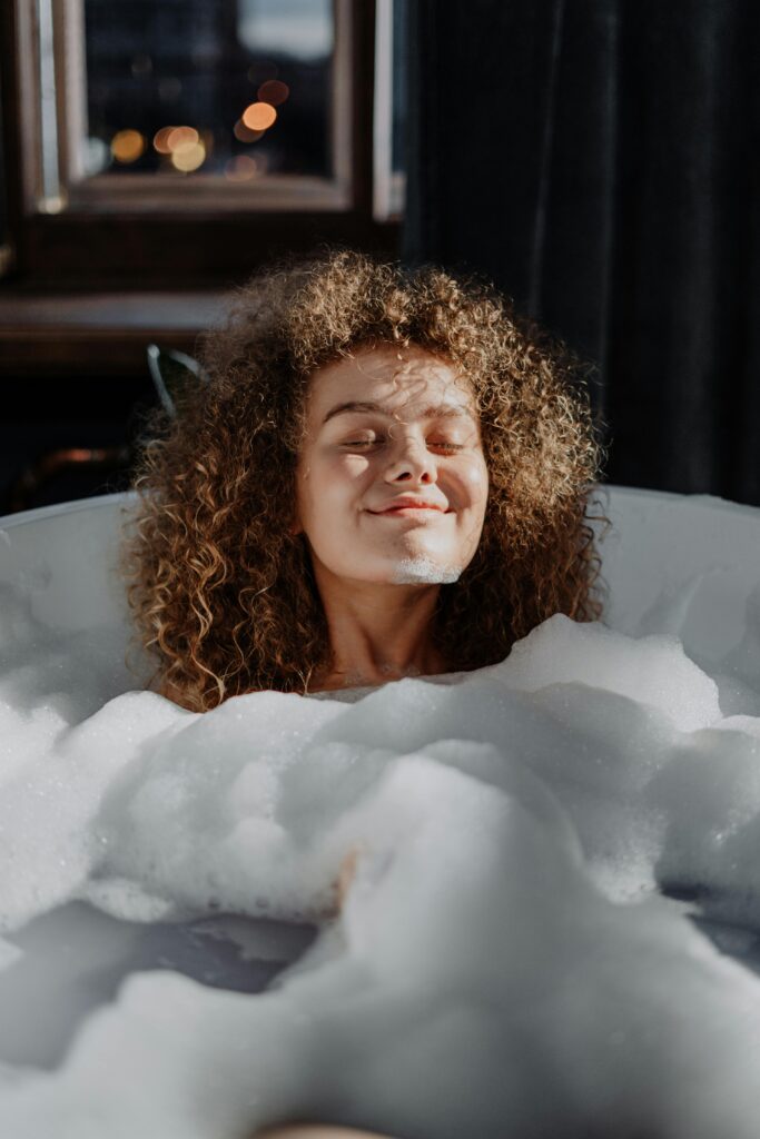 Woman practicing self-care by taking a bubble bath.