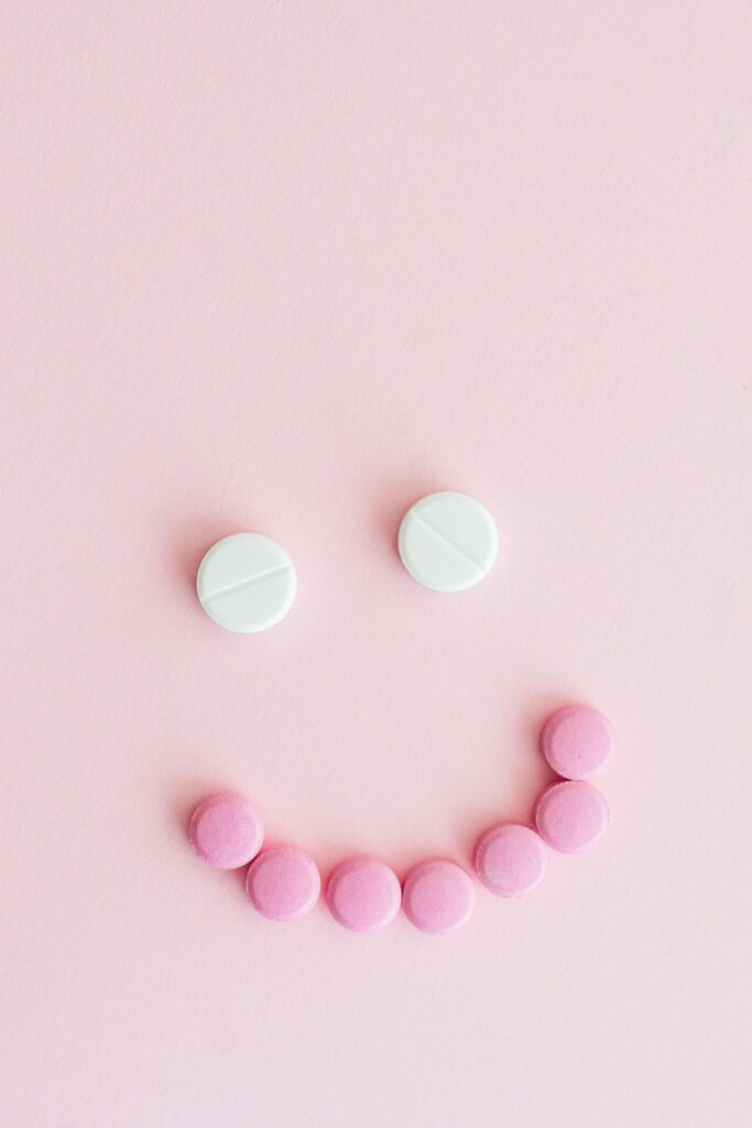 Soft pink background with white and pink pills arranged into a smiling face, symbolizing mental health medication, emotional well-being, and a compassionate perspective on SSRIs and depression treatment.