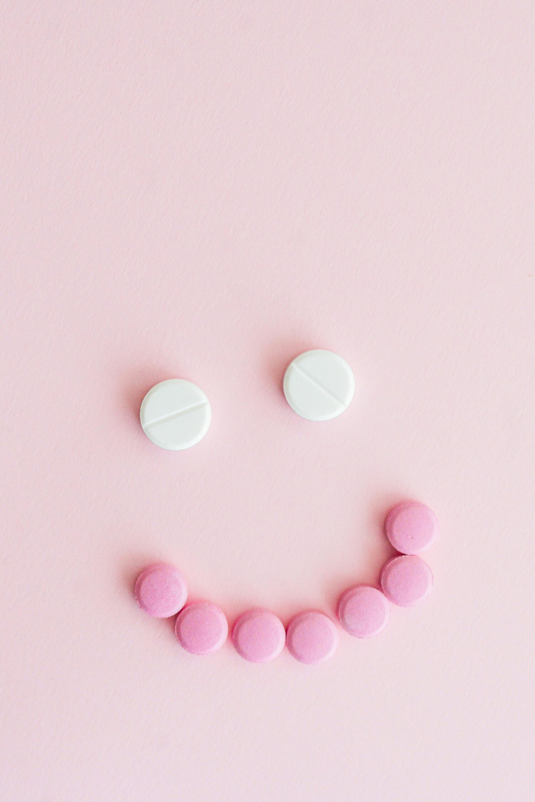 Soft pink background with white and pink pills arranged into a smiling face, symbolizing mental health medication, emotional well-being, and a compassionate perspective on SSRIs and depression treatment.