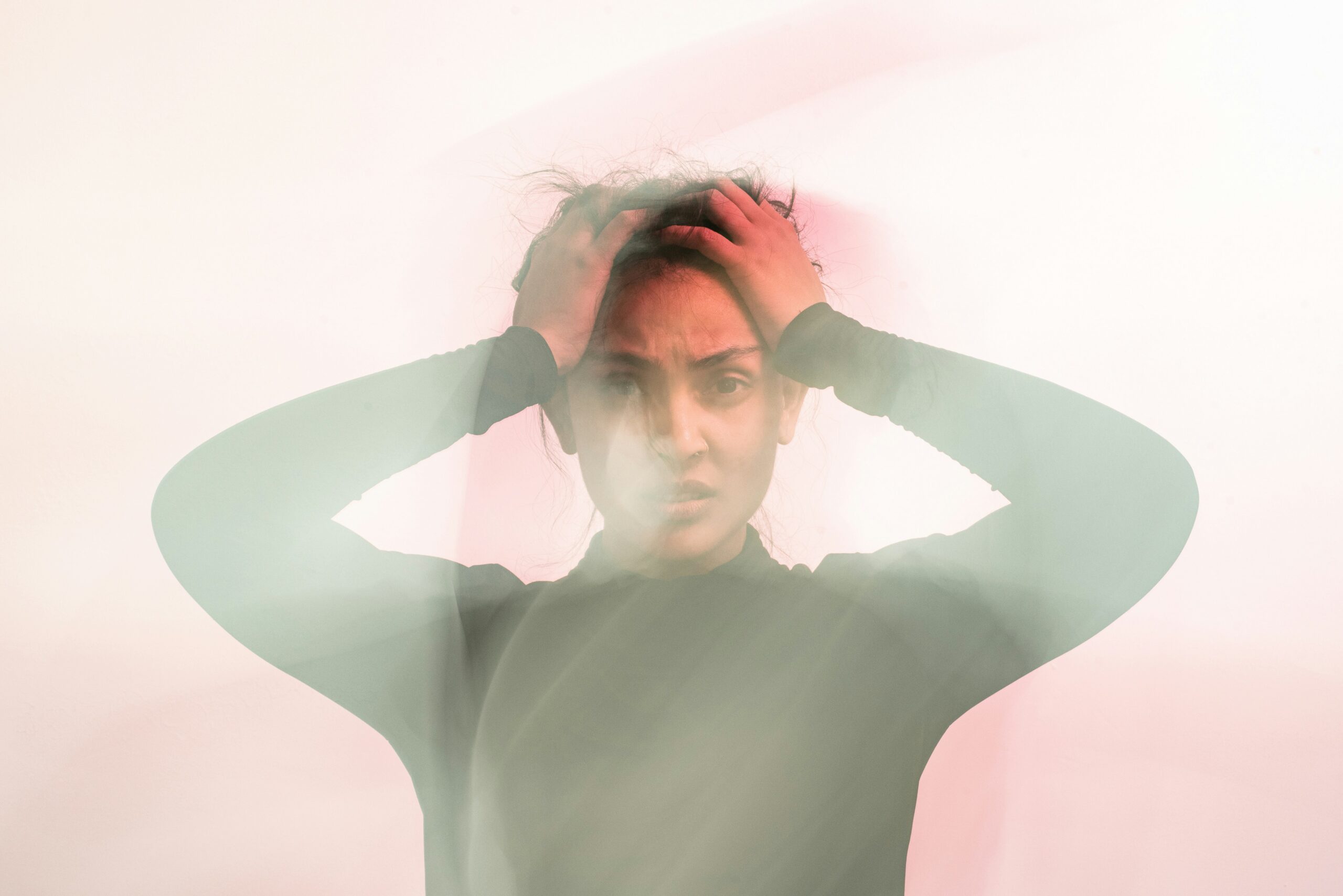 Person holding their head with a blurred double-exposure effect representing anxiety, overwhelm, racing thoughts, and emotional distress.